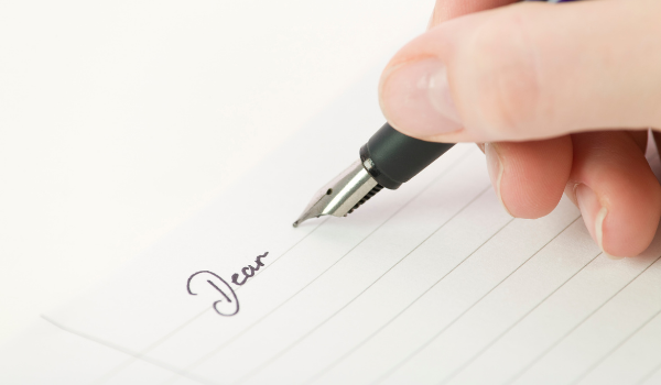 A piece of paper with Dear written in cursive with a hand holding pen. 